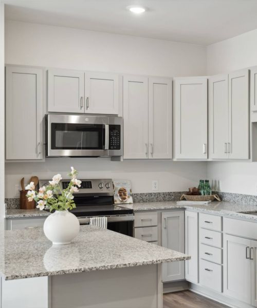 Modern kitchen with white cabinets, granite countertops, stainless steel appliances, and a vase of flowers on island.